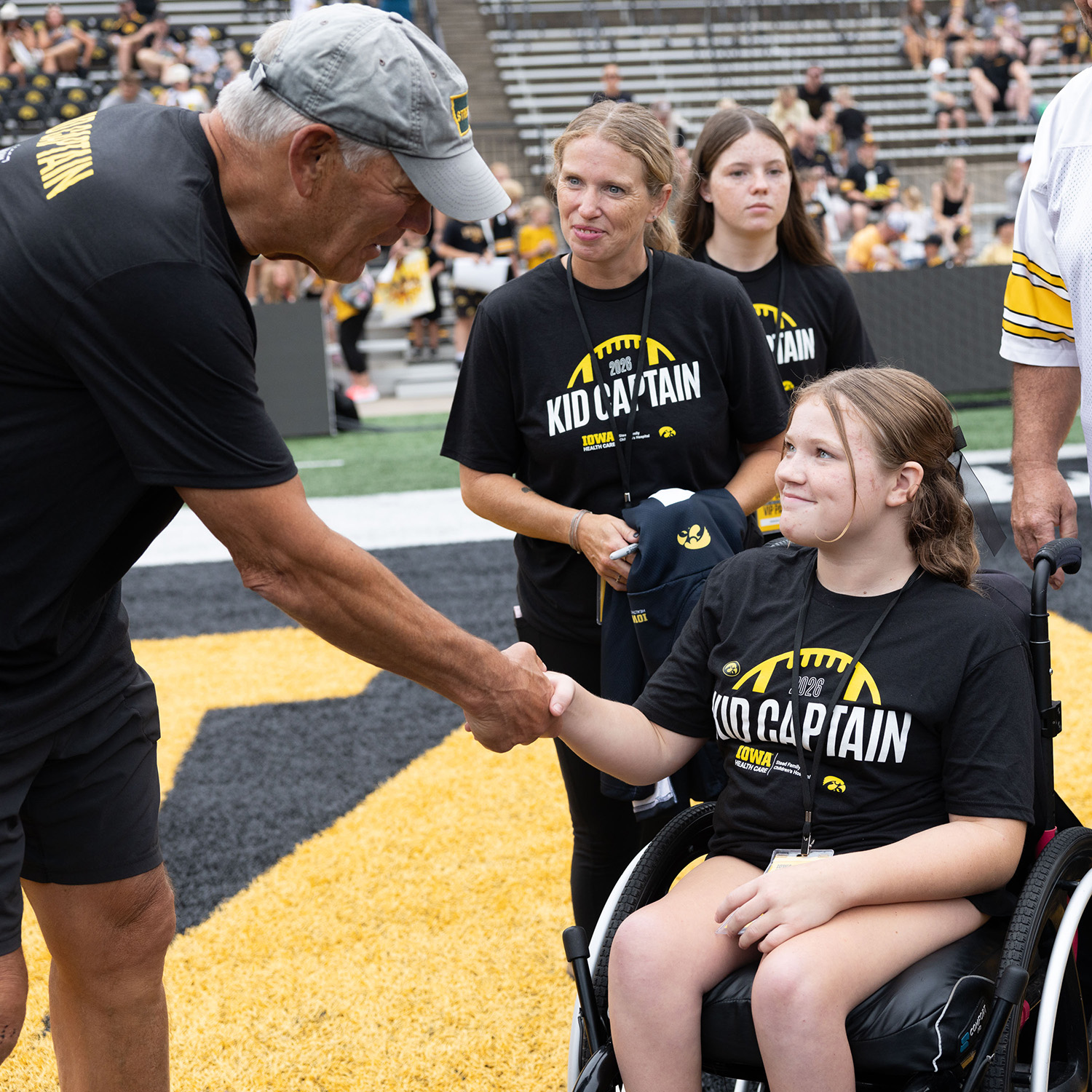 Kid Captain Lily Lee shakes hands with Iowa football coach Kirk Ferentz