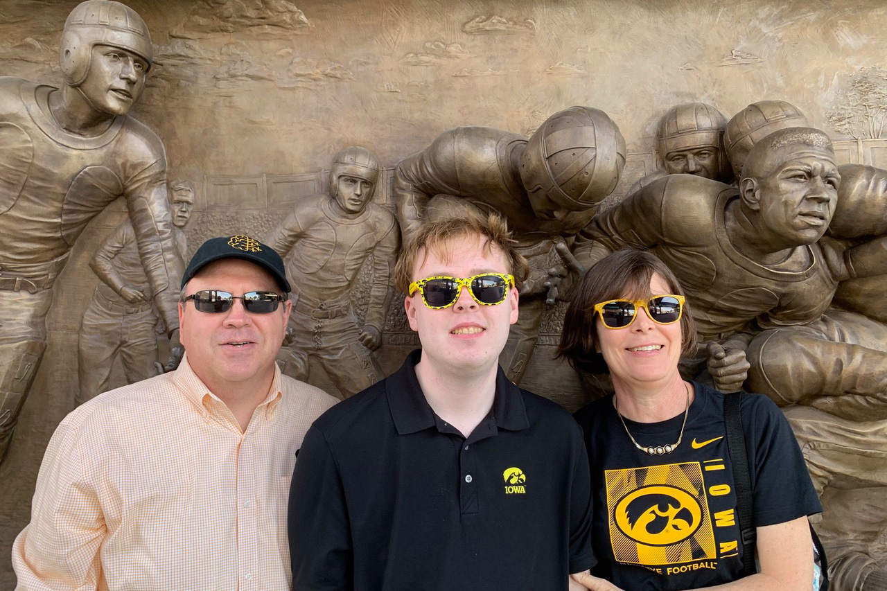 a father and mother stand with their son in front of sculptures of football players outside a stadium