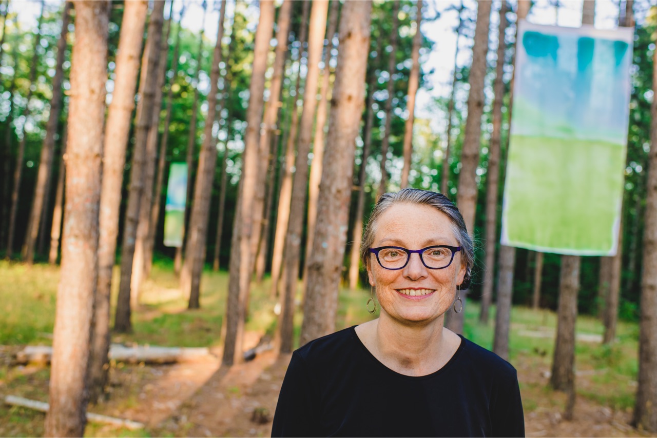 woman in a wooded setting with artwork displayed