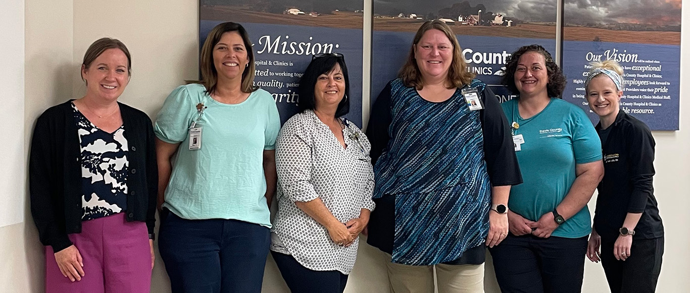 six women pose together in the hallway of a health care facility