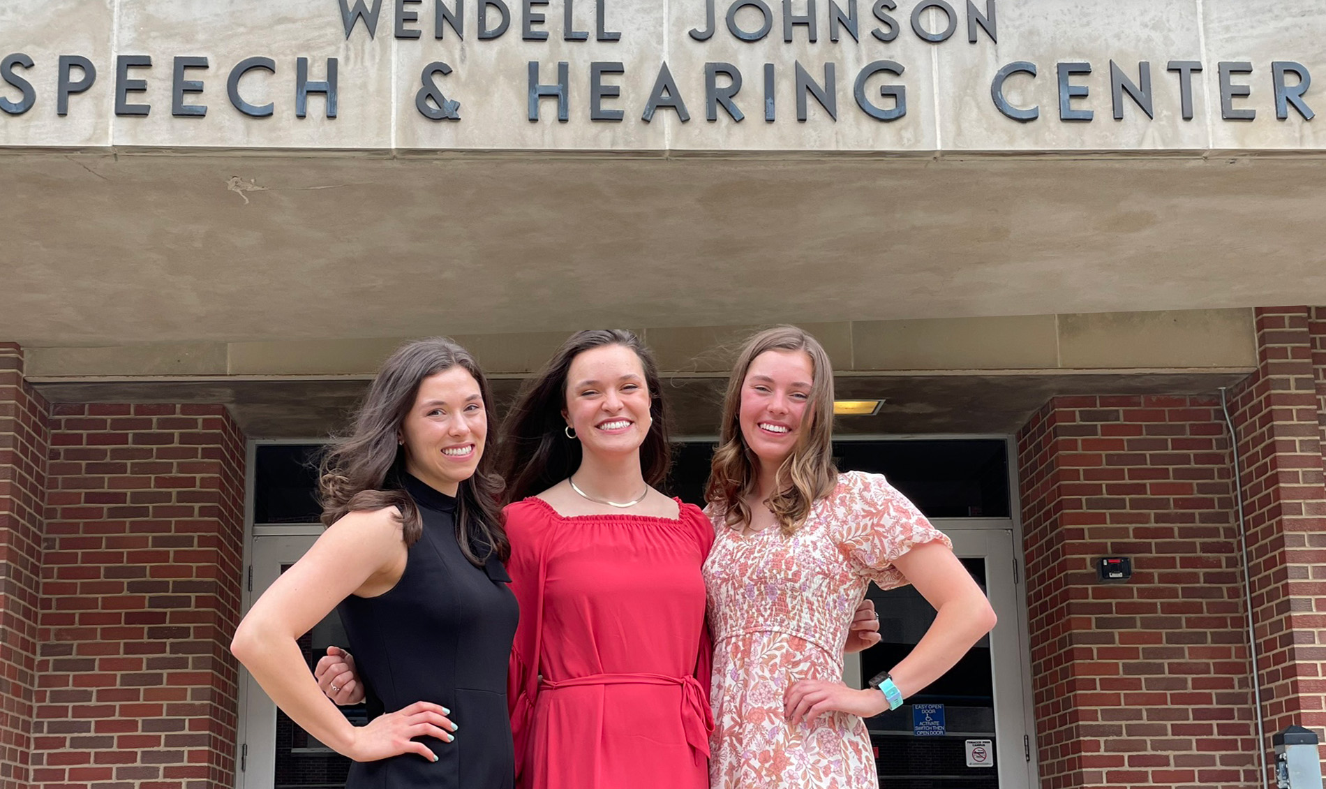 three women stand outside a building