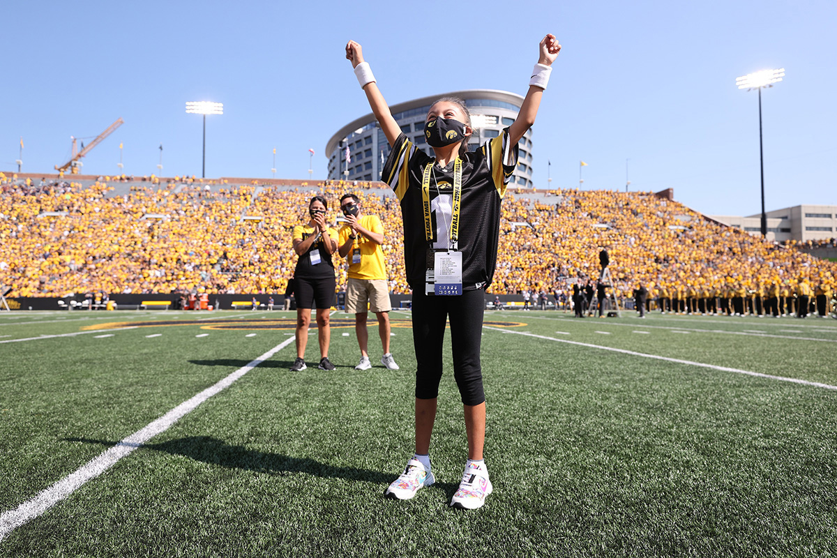 Kid Captain Galilea Gonzalez triumphantly raises both arms while on the field at Kinnick Stadium