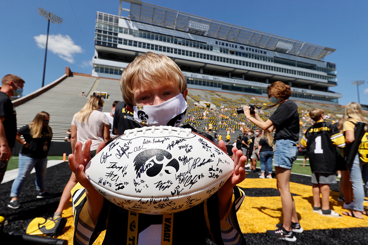 Kid Captain Lucas Moore stands on the field at Kinnick Stadium, holding a football signed by members of the Iowa Hawkeyes football team