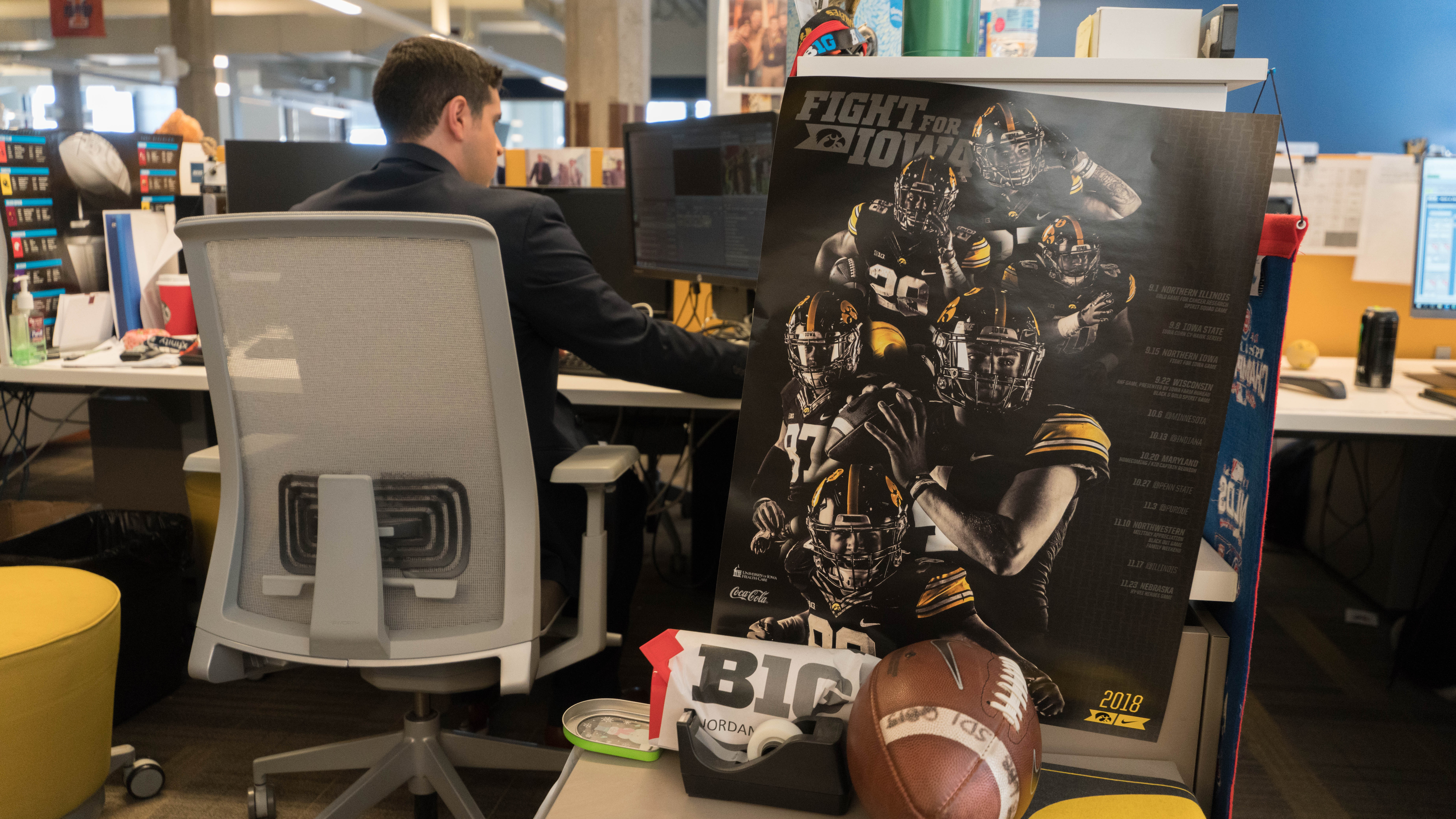 University of Iowa graduate Jordan Loperena at his desk, which features a university of iowa football poster