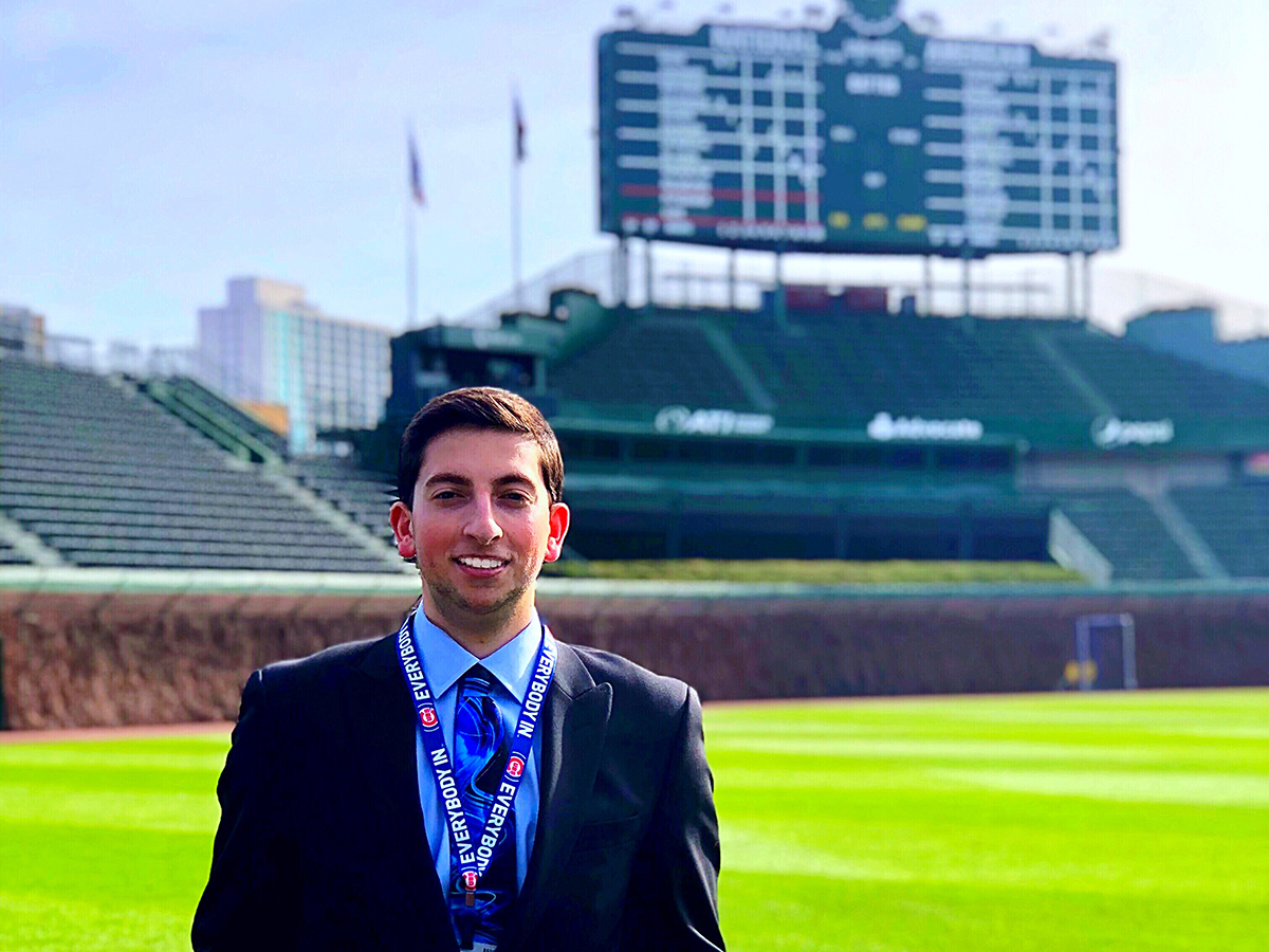 University of Iowa alumnus Jared Mandel standing at Wrigley Field with the iconic scoreboard in the background