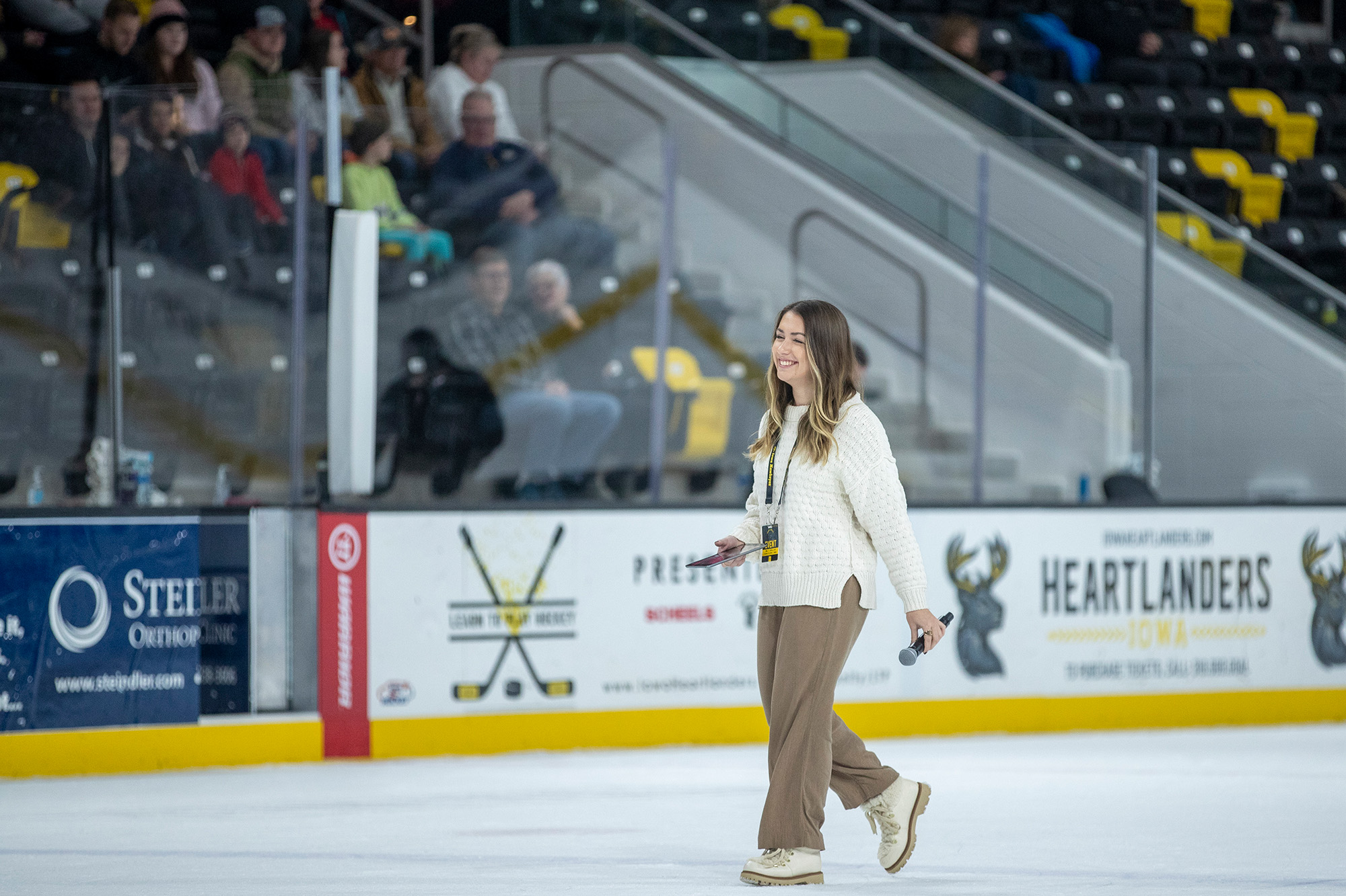a woman walking on the ice of a hockey rink, smiling and holding a microphone