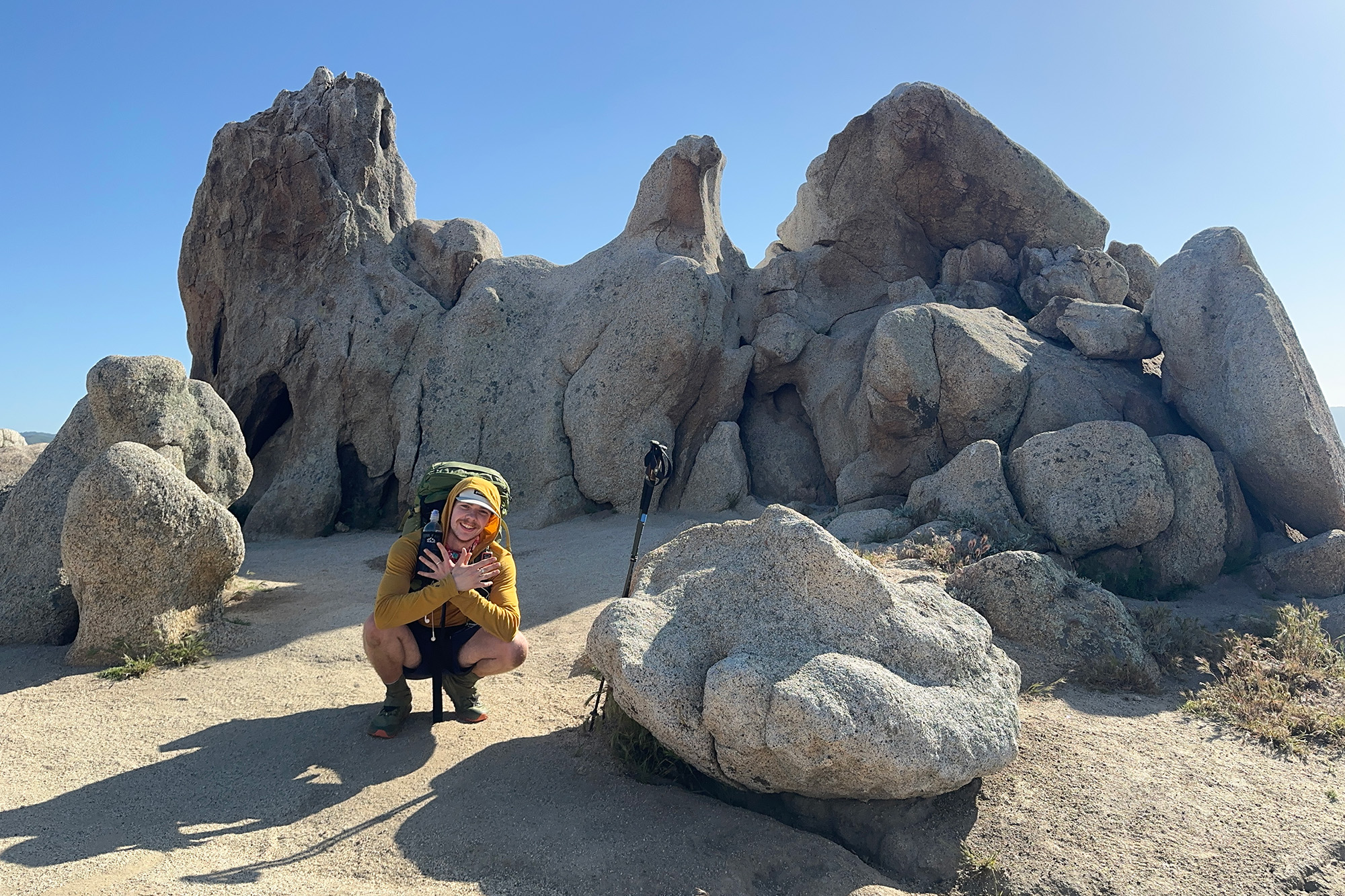 a man crouching near some large rocks near a hiking trail