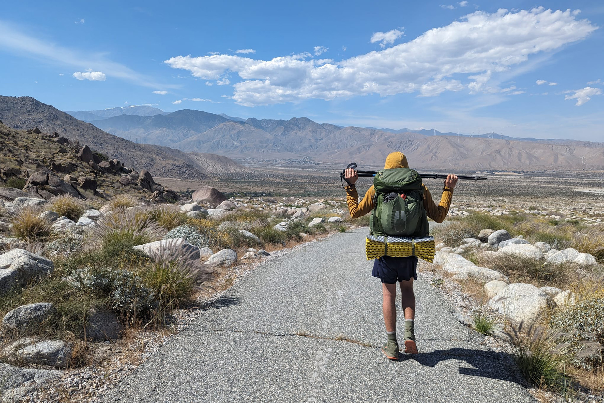 a man walking on a hiking trail with mountains in the background