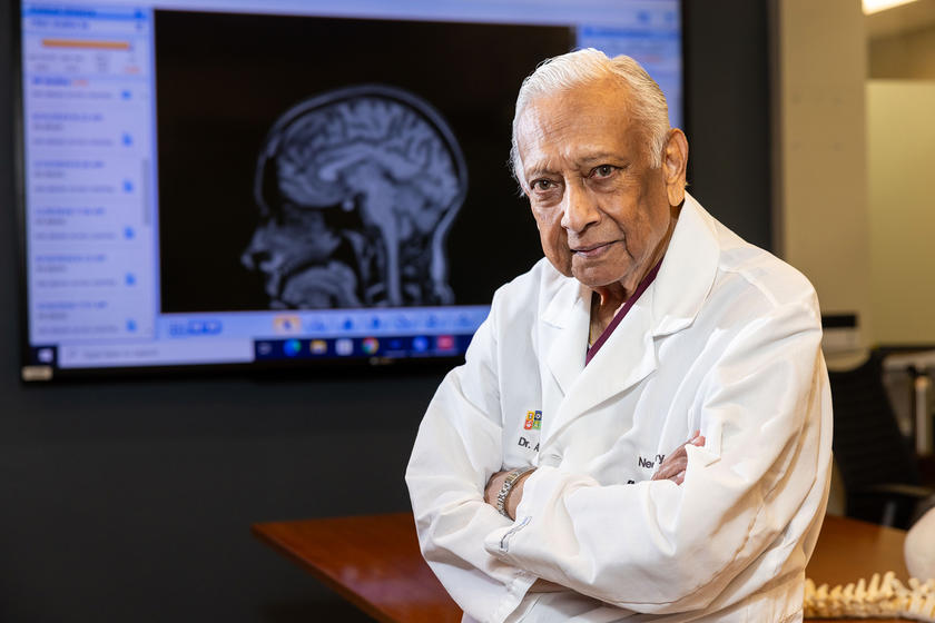 neurosurgeon Arnold Menezes in a room with a brain image on a presentation screen in the background