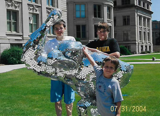three boys standing by a reflective statue of Herky