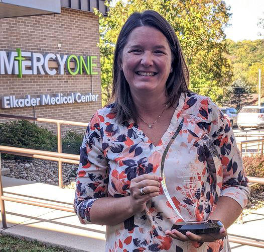 a woman holds an award while standing outside a rural health care facility