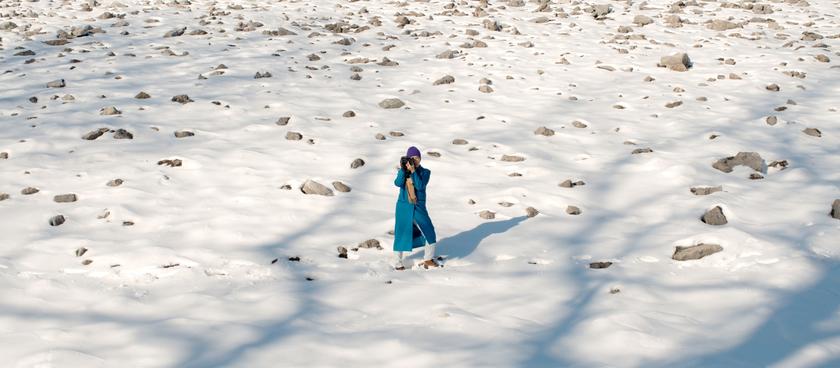 a still image from Hao Zhou's film Frozen Out, in which Zhou is seen off in the distance, standing in a snowy area holding a camera, looking upward