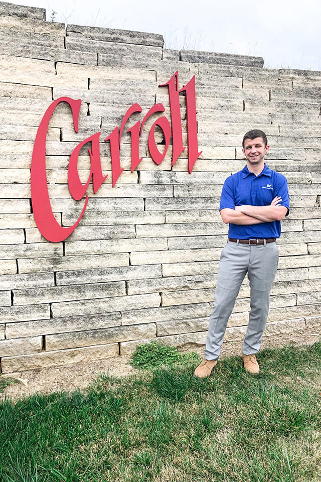 University of Iowa medicine grad Taylor Hircock standing near a sign with the town name Carroll