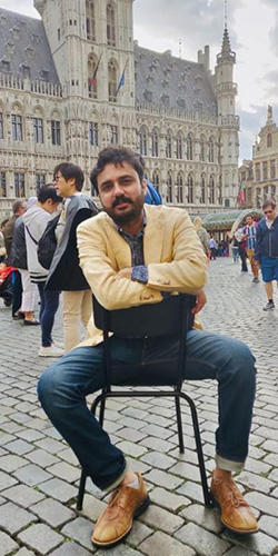 Iowa Playwrights Workshop student Ikram Basra sitting on a chair on a crowded plaza