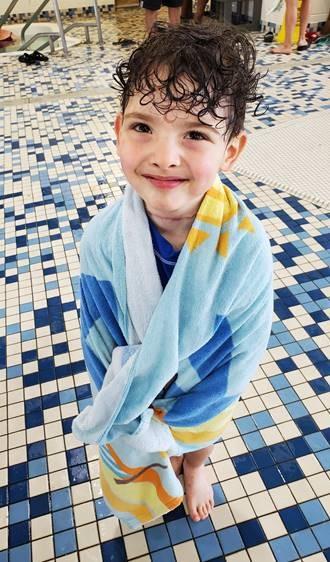 a young boy stands poolside wrapped in a towel