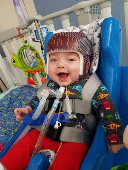 a young boy sits in a health care setting, wearing protective headwear