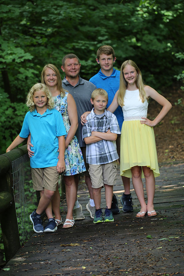 a family of six stands in an outdoor setting, posing for a photo