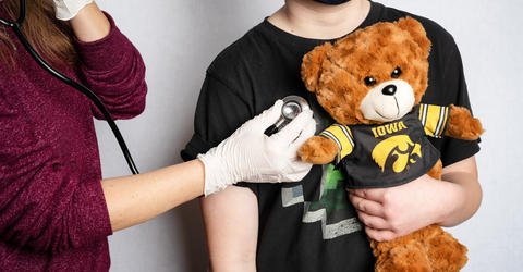A child is examined while holding a teddy bear