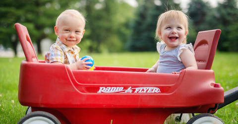 two young children smiling while sitting in a red wagon