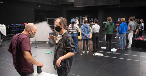 Iowa Playwrights Workshop graduate Dakota Parobek (foreground, right) speaks with director Paul Kalina on the set of Smile Medicine, written by Parobek and part of the University of Iowa's Mainstage 2021-22 theater season