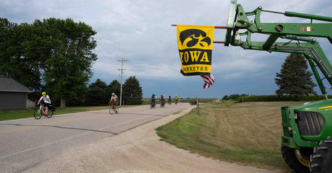 RAGBRAI riders pass by farm equipment flying an Iowa Hawkeyes flag