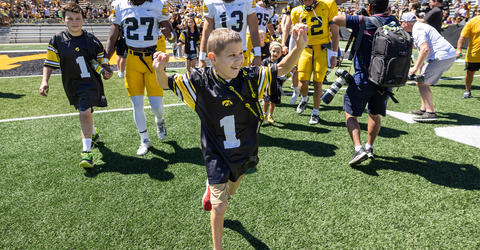 Kid Captain Wyatt Rannals walks on a football field with both arms raised