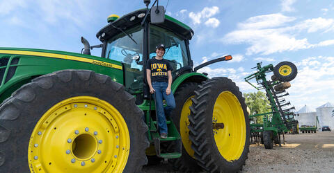 University of Iowa alumna and grad student Aubrey McEnroe stands on a tractor on her family farm