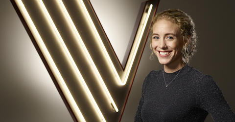 University of Iowa alumna Cali Wilson standing before a logo for The Voice