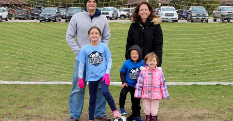 a family of five standing in front of a soccer goal