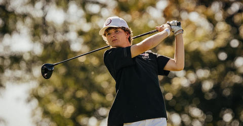 a young man swinging a golf club on a tee box