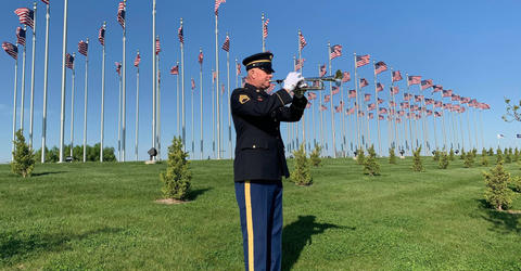 Jeff Six playing the trumpet outdoors, in front of numerous flag poles with US flags flying