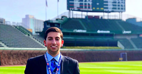 University of Iowa alumnus Jared Mandel standing at Wrigley Field with the iconic scoreboard in the background