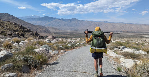 a man walking on a hiking trail with mountains in the background