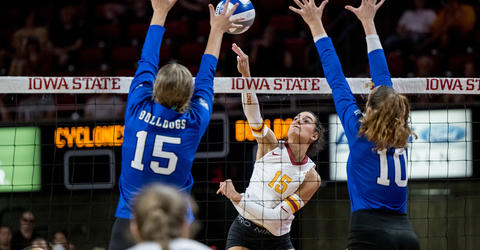 Iowa State University volleyball player Kiersten Schmitt rises up to hit the ball as two opponents attempt to block the shot