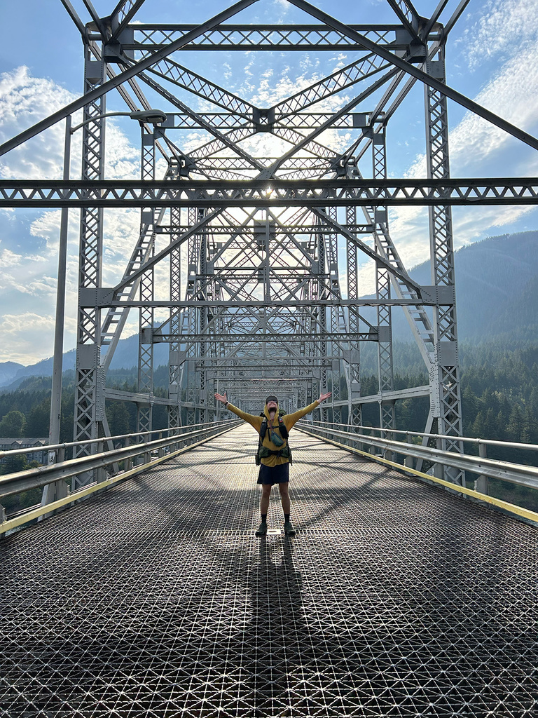 a man raising his arms in triumph while standing on a bridge on the Pacific Crest Trail