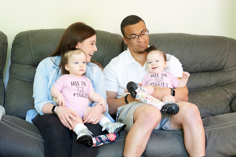 twin girls sitting on the laps of their parents, who are sitting on a couch
