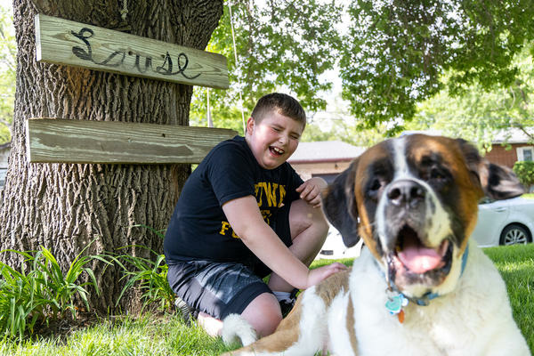A boy outside playing with his puppy and laughing