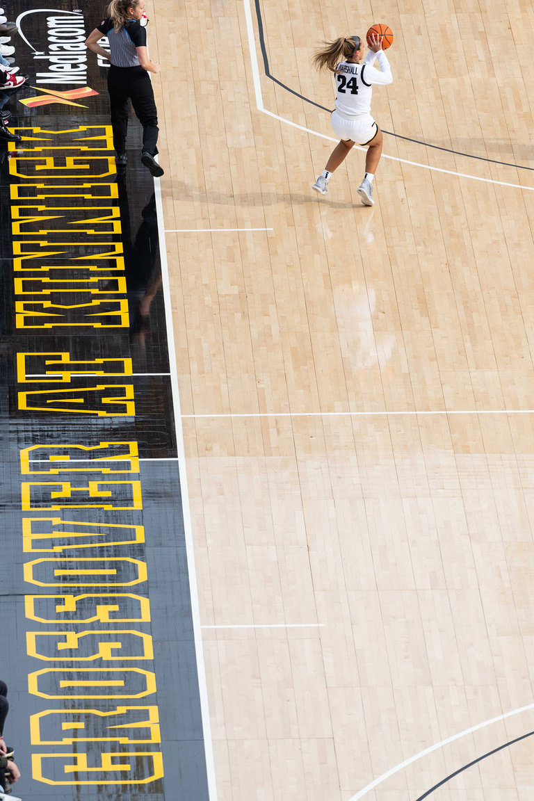 Gabby Marshall shooting a three-pointer during Crossover at Kinnick; the name of the game is printed on the sideline behind her
