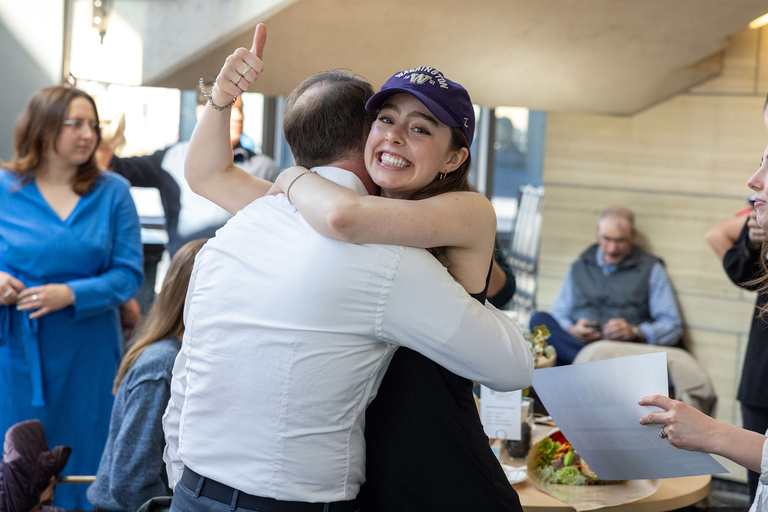 A woman hugging someone while smiling and giving a thumbs-up
