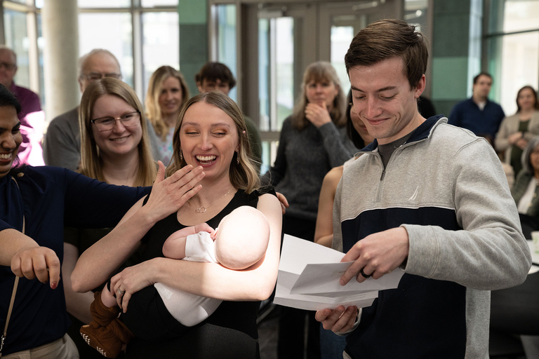 A woman holding a baby as a man opens a letter