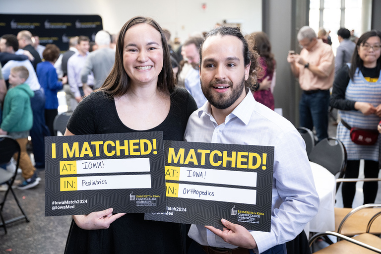 Two people holding up signs declaring where they matched
