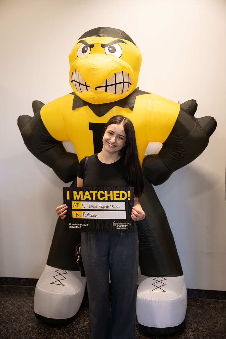 A woman hoding a sign saying where she matched standing in front of an inflatable herky