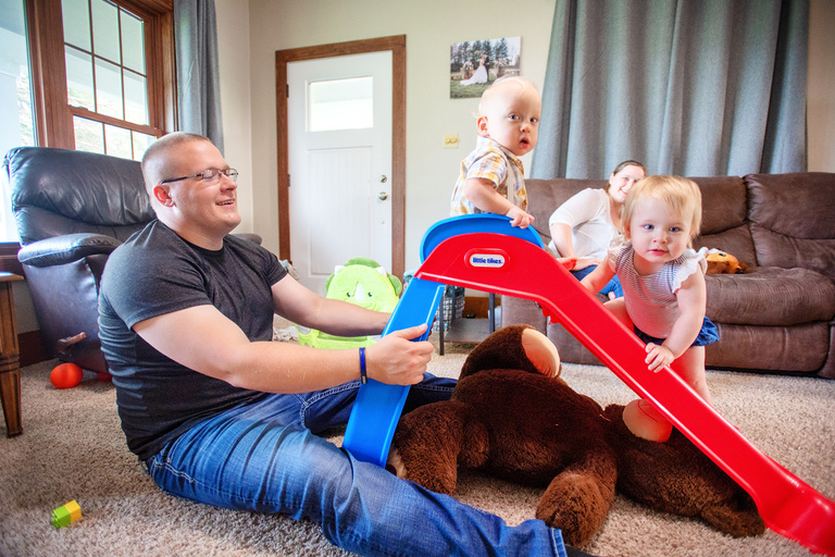 a father holding onto a toy slide while his children play on it