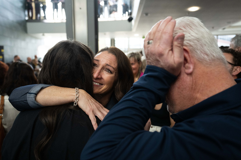 Two people hugging while a man wipes his eyes