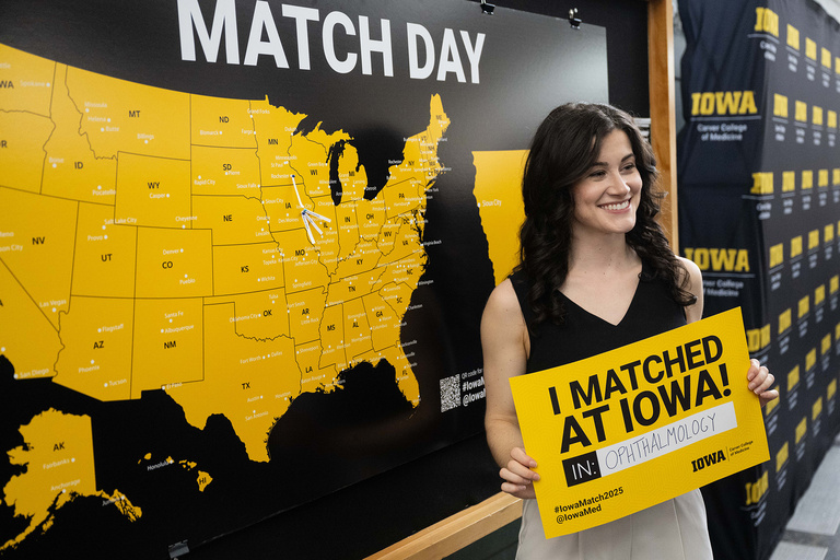 A map with a lot of pins on it and a woman holding a sign standing in front of it