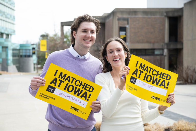 Two people holding up signs indicating their work at Iowa