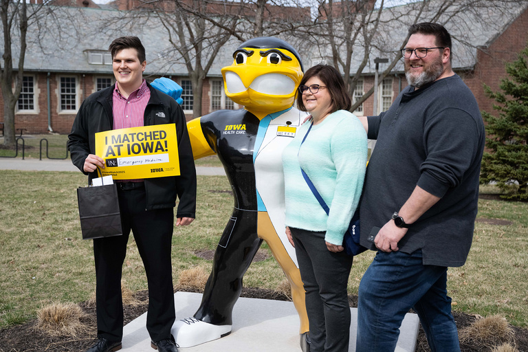 Three people smiling standing around a statue of Herky