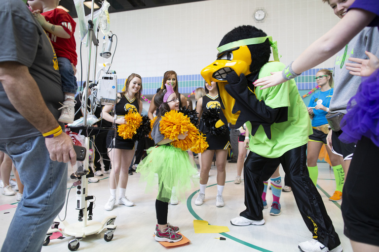 Herky and a group of cheerleaders dancing with a young girl
