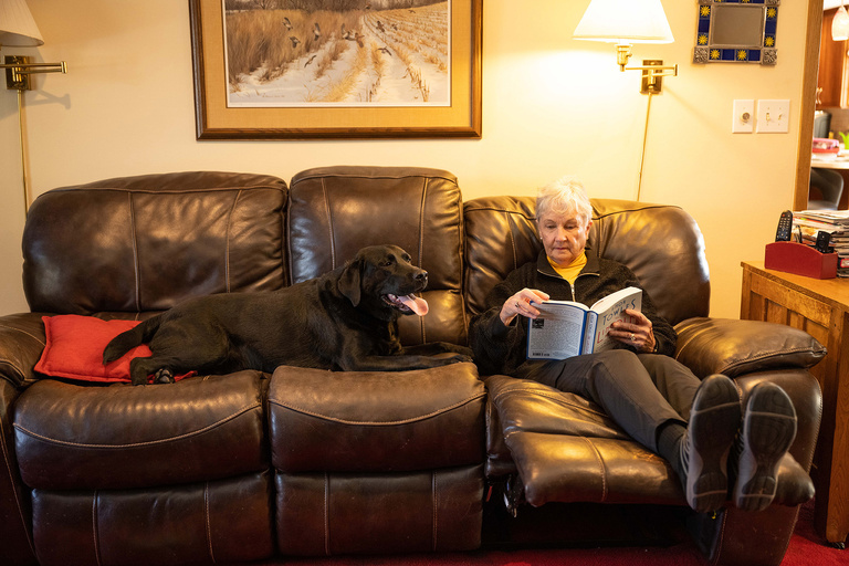 a woman reading while sitting on a couch with her doggo