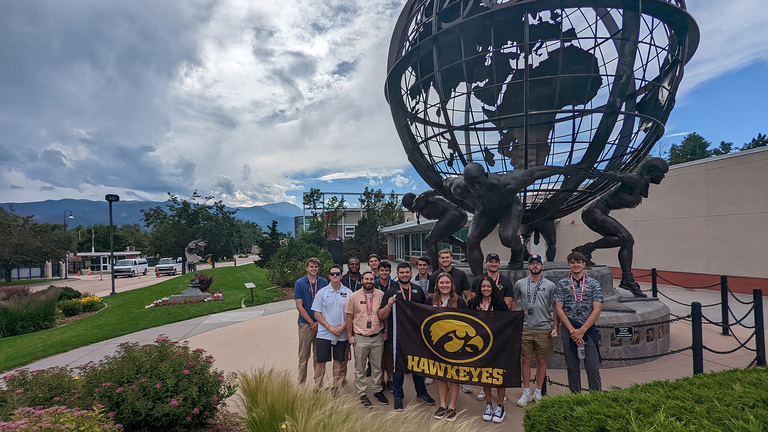 students holding a tiger hawk flag while standing in front of a globe statue